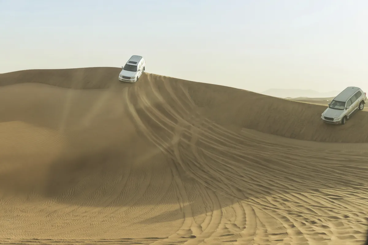Zwei Geländewagen fahren über einen Dünenkamm in der Wüste bei Dubai
