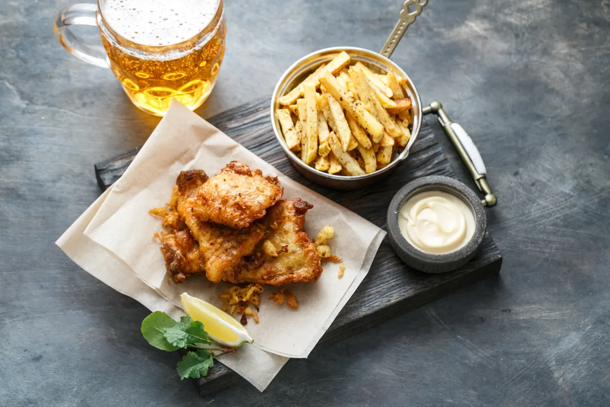 Fish and Chips auf Papier mit einer Schale Pommes und einem Glas Bier