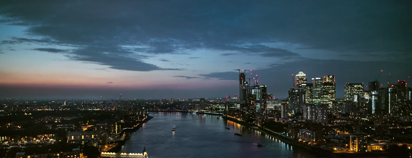 Die Themse in der Abenddämmerung von oben, rechts die beleuchteten Hochhäuser von Canary Wharf
