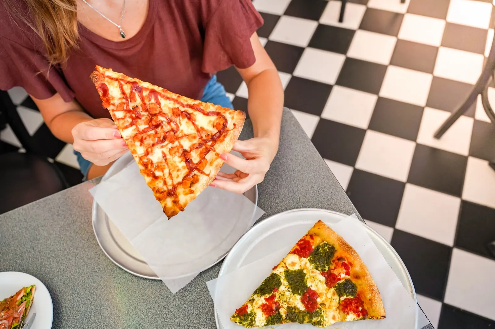 Hände nehmen ein Stück Pizza von einem Teller auf einem Restauranttisch