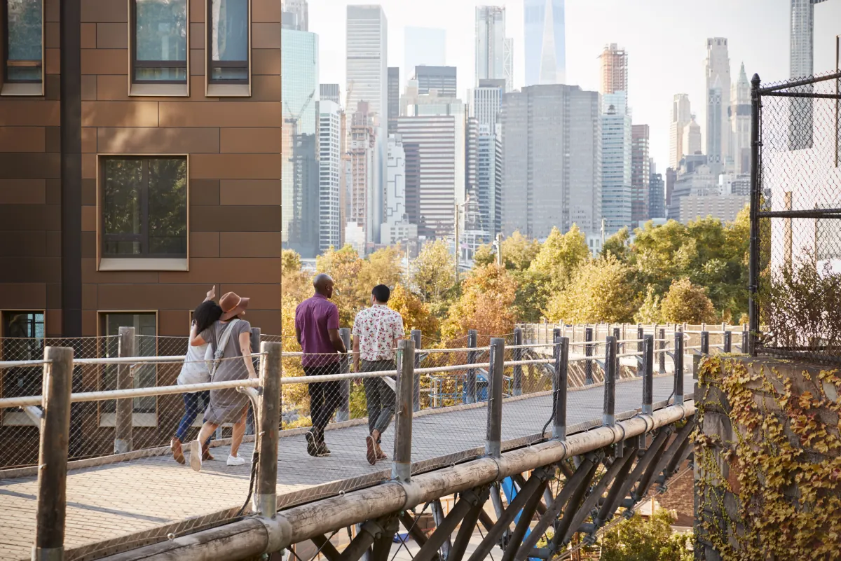 Menschen gehen über einen erhöhten Fußweg, im Hintergrund die Hochhäuser von Manhattan