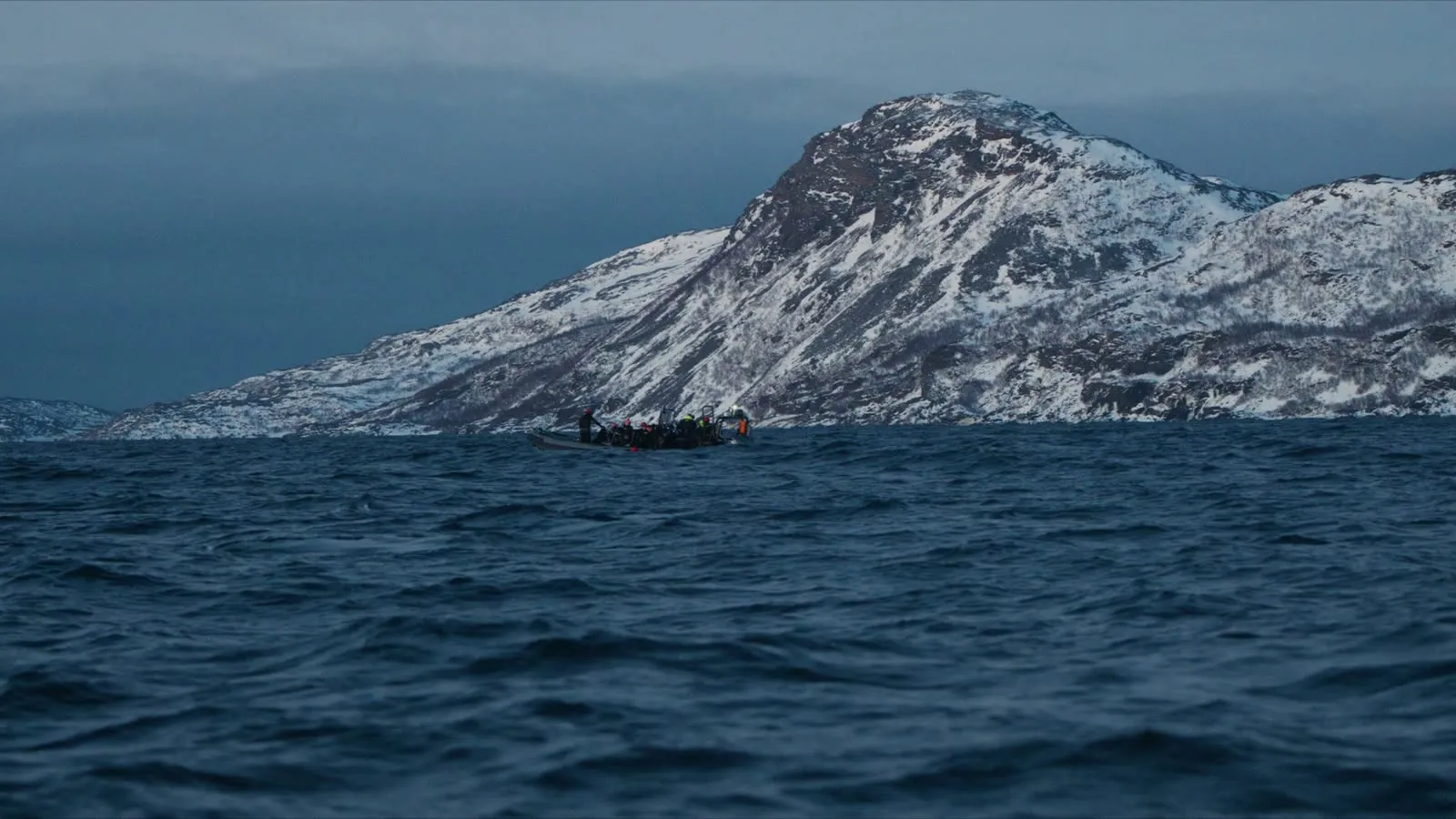 Expeditionsschiff fährt durch einen arktischen Fjord unterhalb verschneiter Berge in Nordnorwegen