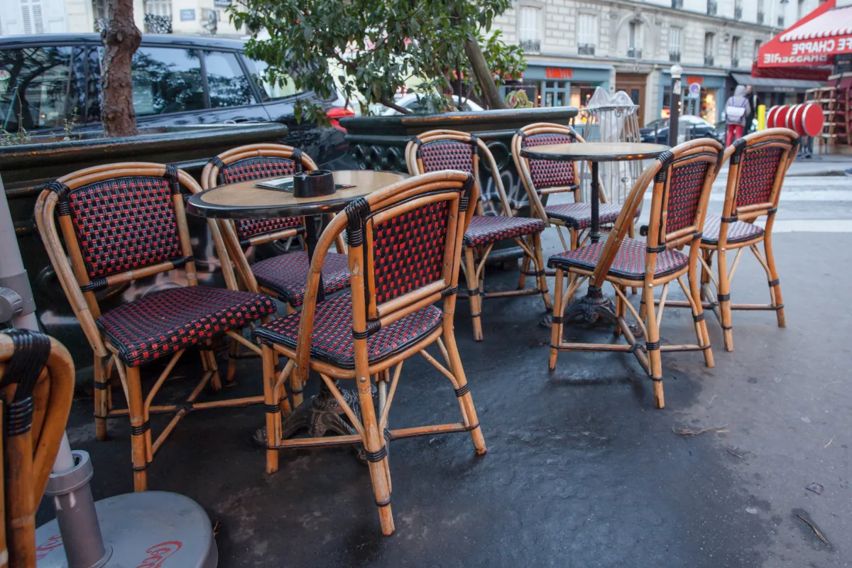 Leere Bistrostühle aus Rattan auf einer Pariser Straße zwischen zwei Servicezeiten