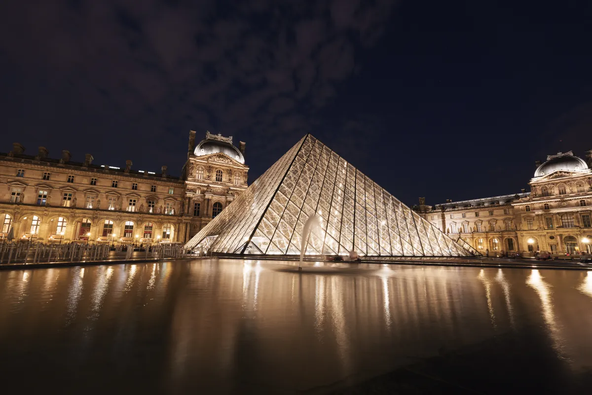 Die beleuchtete Glaspyramide im Innenhof des Louvre bei Nacht, gespiegelt im Wasserbecken