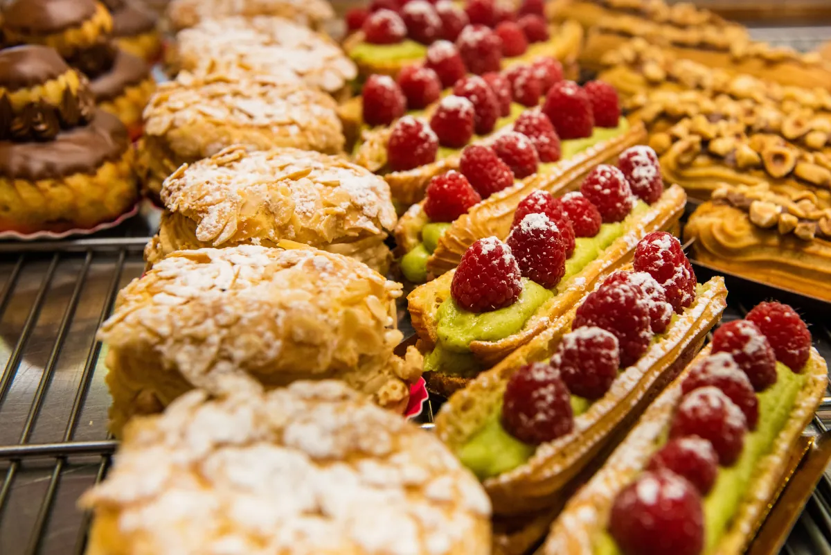 Eclairs und Törtchen mit Himbeeren und Mandeln in der Auslage einer Patisserie