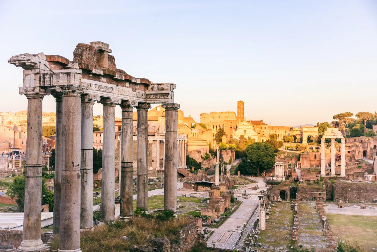 Die Säulen des Saturntempels im Forum Romanum bei Sonnenaufgang, dahinter das Kolosseum