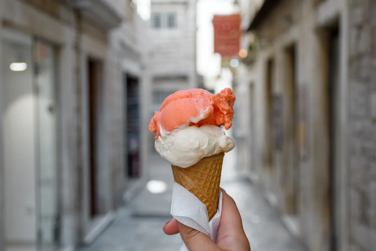 Eine Hand hält eine Eiswaffel mit zwei Kugeln in einer engen Altstadtgasse